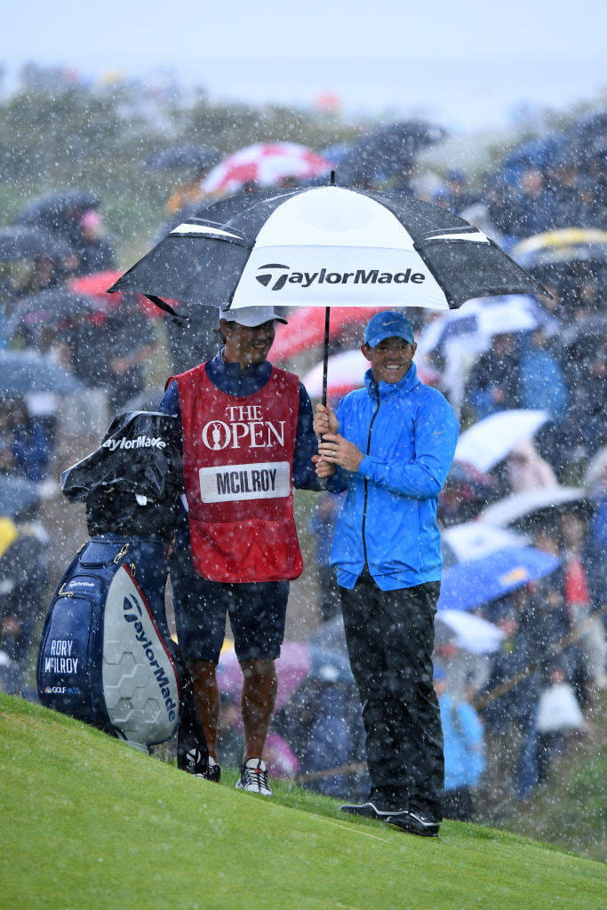 Rory McIlroy shielding with his caddie under an umbrella from rain